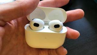 Karanlık bir masanın yanında tutulan Apple AirPods 3