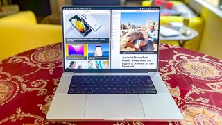 MacBook Pro 2021 (16 inç), iki web sayfasını yan yana gösteren bir masa üzerinde duruyor