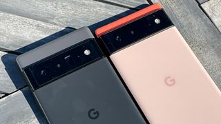 Ahşap zemin üzerinde yan yana yerleştirilmiş Google Pixel 6 Pro (siyah) ve Google Pixel 6 (mercan)