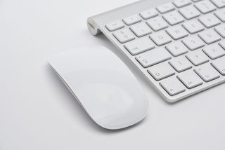 Beyaz bir yüzey üzerinde beyaz ve gri bir Apple Magic Klavyenin yanında beyaz bir Apple Magic Mouse