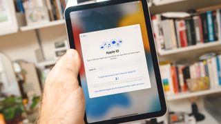 Ekranda Apple Kimliği giriş sayfası olan ve Apple Kimliği e-posta adresinizi nasıl değiştireceğinizle ilgili bir makaleyi temsil eden bir iPad tutan kişi