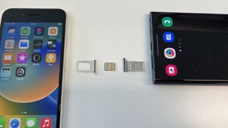 SIM tepsileri çıkarılmış ve aralarına bir nano SIM kart yerleştirilmiş bir iPhone SE 2022 ve bir Samsung Galaxy S22 Ultra