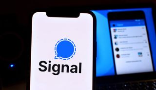 Bir iPhone'da görüntülenen Signal uygulaması logosu ve arka planda bir monitörde kullanılan Signal uygulamasının ekran görüntüsü.