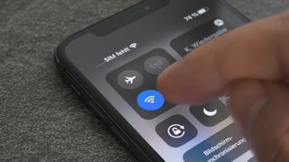 iPhone'da bir Wi-Fi ortak erişim noktasının nasıl kurulacağına ilişkin bir makaleyi temsil eden, Kontrol Merkezi'ndeki Wi-Fi düğmesine dokunan bir parmağı gösteren bir iPhone görüntüsü