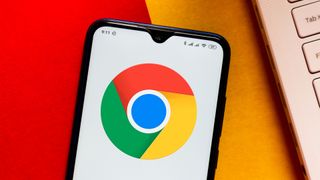 Turuncu ve kırmızı bir yüzey üzerinde duran bir Android akıllı telefonda görüntülenen bir Google Chrome logosu