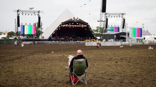 Glastonbury Müzik ve Sahne Sanatları Festivali'nin son gününde eğlence tutkunları uyanırken bir adam Pazar gazetesini okuyor.