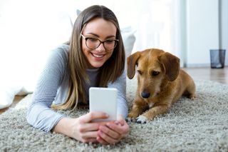 Akıllı telefona bakan halının üzerinde oturan kadın ve köpek