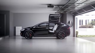 Beyaz bir garajda bir ev şarj cihazının yanında oturan Siyah Tesla Model Y