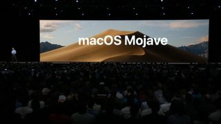 Ekranda macOS Mojave görüntüsüyle konferansta sunum yapan adam