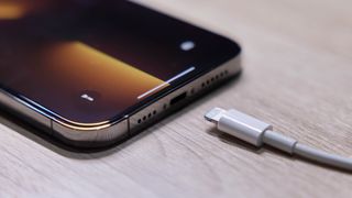 Şarj bağlantı noktasının yanında Lightning kablosu bulunan bir masada iPhone 13