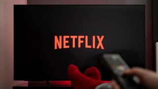 TV ekranında ayaklar yukarıda ve uzaktan kumandayı tutan Netflix