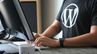 WordPress tişörtüyle bilgisayar başında çalışan adam