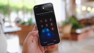 Kilit ekranı sayısal tuş takımını gösteren bir iPhone tutan kişinin görüntüsü