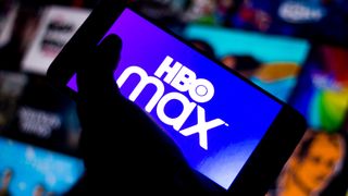 Diğer ekranların önünde karanlıkta elle tutulan bir telefonda HBO Max logosu