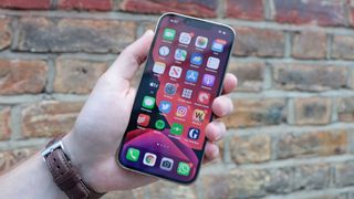 Arka planda bir tuğla duvarla birinin elinde tutulan bir iPhone 13 Pro